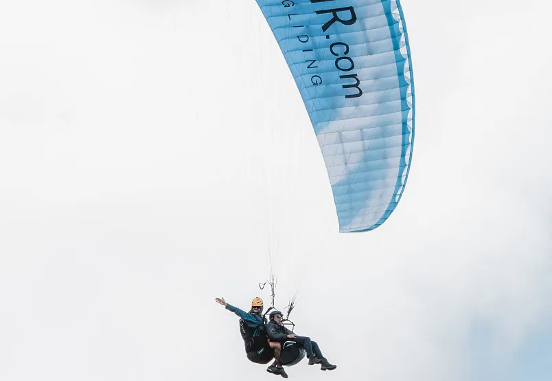 Zwei Personen beim Paragliding unter einem blauen Schirm in der Luft.