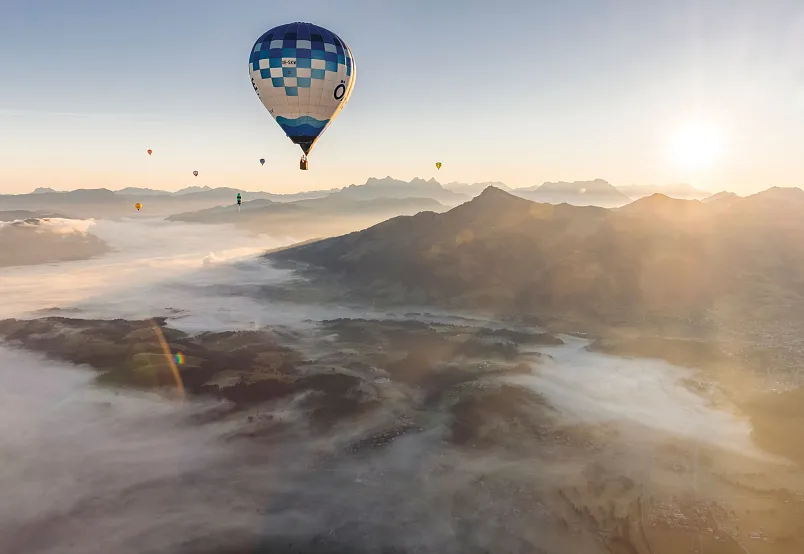 Hot air balloons floating over a foggy mountain landscape at sunrise.