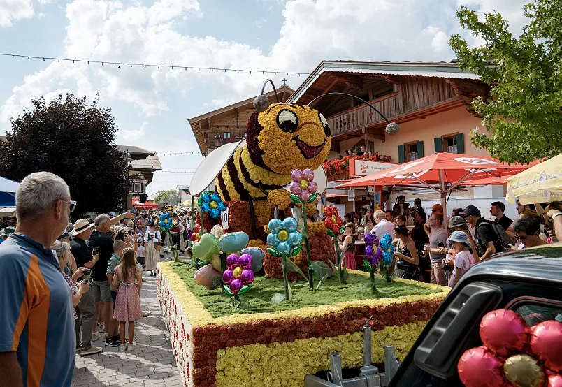 Colorful bee-themed float with flowers in a lively outdoor festival setting.