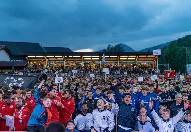 A large group of people in sports attire gathered outdoors in front of a building, some holding signs and cheering.