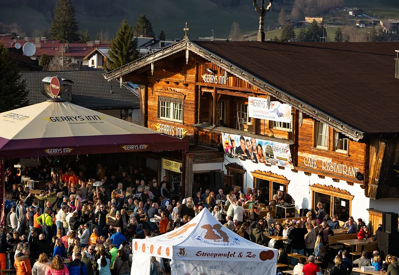 Large crowd gathered outside a traditional Alpine chalet with wooden facade in a bustling outdoor event.