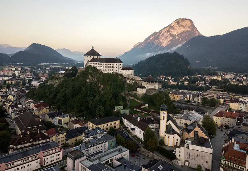 Luftaufnahme einer Stadt in Tirol mit einer Festung auf einem Hügel, umgeben von Bergen.