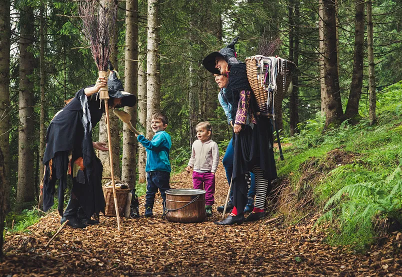 Kinder treffen im Wald auf zwei als Hexen verkleidete Frauen, die einen Hexenkessel und Besen haben.