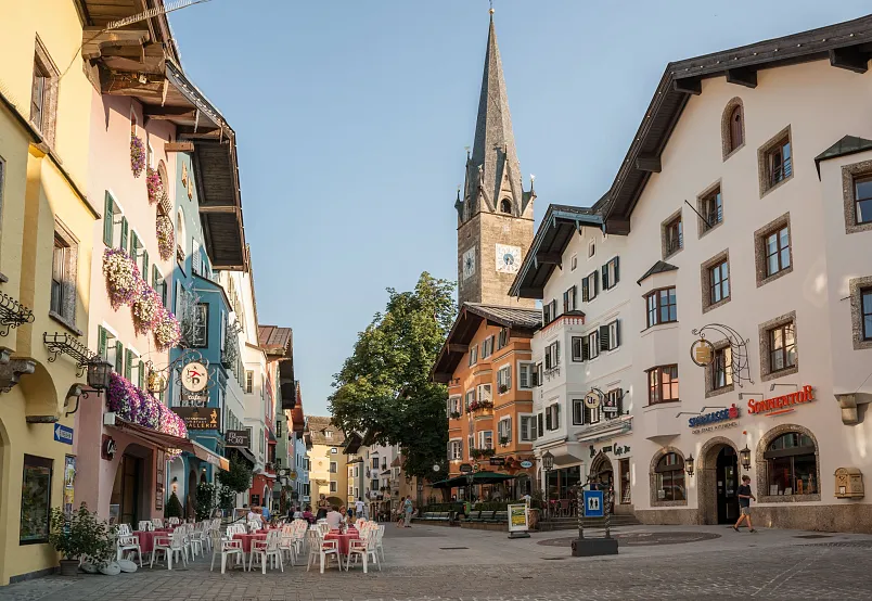 Malerische Altstadt von Kitzbühel mit bunten Gebäuden und einem Kirchturm bei klarem Himmel.