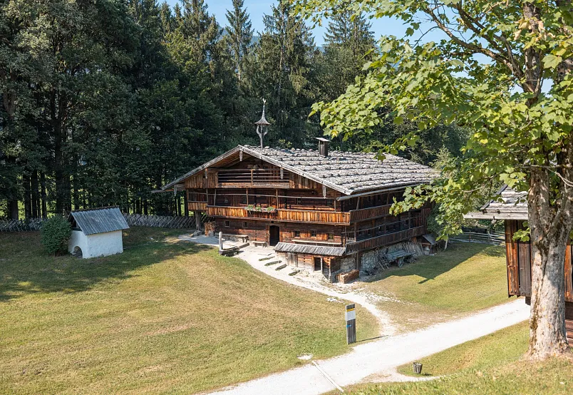 A traditional wooden chalet surrounded by trees in a sunny landscape.