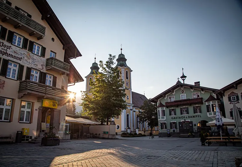 Historischer Marktplatz in Kitzbühel mit Kirche und traditionellen Gebäuden bei Sonnenuntergang.
