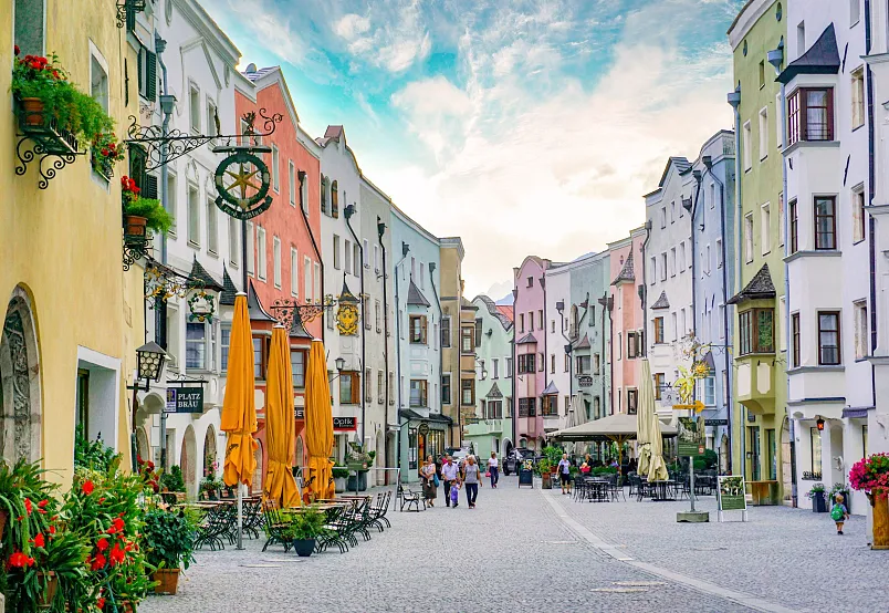 Bunte Häuserfassade und Café-Terrassen in einer charmanten Altstadt, bevölkert von Menschen, bei Tageslicht.