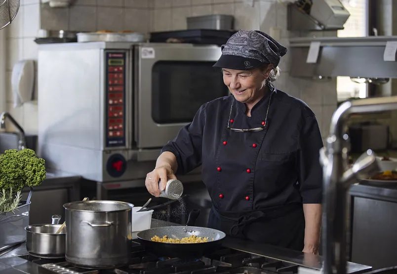 Köchin in schwarzer Uniform würzt Essen in einer professionellen Küche.