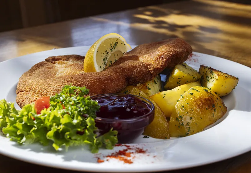 Ein Wiener Schnitzel mit Kartoffeln, Preiselbeersauce und Salat auf einem weißen Teller.
