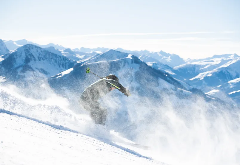 Skifahrer fährt bei Sonnenschein eine verschneite Alpinpiste in den Alpen hinab.