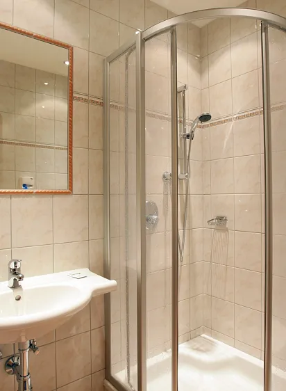 Moderne badkamer met glazen douche, wastafel en spiegel op beige betegelde muren.