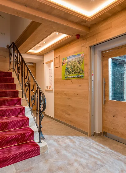 Holzverkleideter Hotelkorridor in Tirol mit rotem Teppich auf der Treppe und einem Willkommensschild.