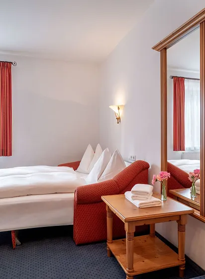 Gemütliches Hotelzimmer in Kitzbühel mit Doppelbett, Sitzbereich und großem Spiegel, in warmen Tönen dekoriert.