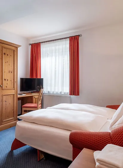 Gemütliches Hotelzimmer in traditionellem Design mit Holzmöbeln, Doppelbett und einem kleinen Schreibtisch mit Fernseher.