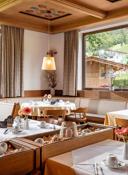 Gemütliches Restaurant mit Holztischen und großen Fenstern mit Blick auf eine alpine Landschaft.