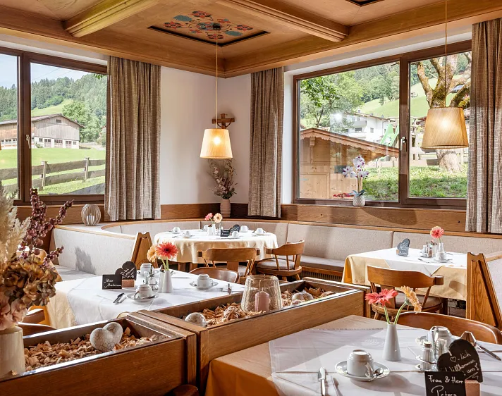Gemütliches Restaurant mit Holztischen und großen Fenstern mit Blick auf eine alpine Landschaft.