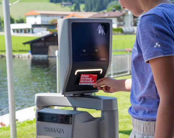 Person an einem elektronischen Ticketscanner im Freien in einer alpinen Umgebung.