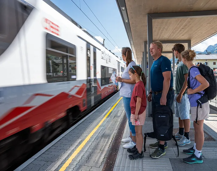 Gruppe von Menschen steht auf einem Bahnsteig, während ein Zug vorbeifährt.