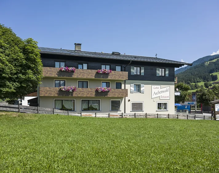 Traditionelles Gasthaus in Tirol mit Blumenkästen an den Balkonen und den Kitzbüheler Alpen im Hintergrund.