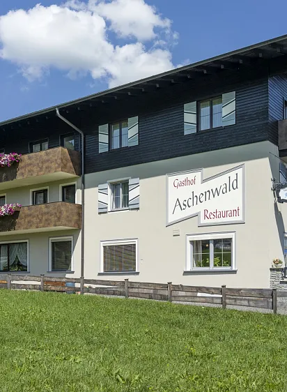 Gasthof Aschenwald in Westendorf mit blühenden Blumenkästen vor grünem Hintergrund.