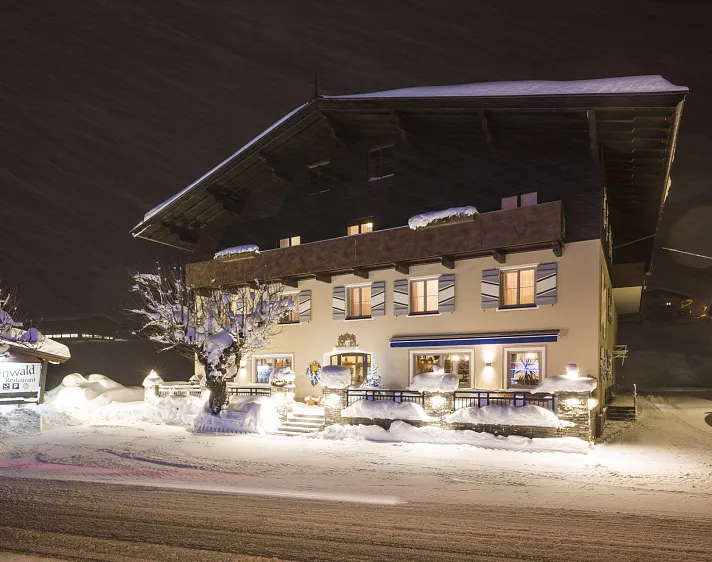 Ein verschneites Gasthaus in Tirol bei Nacht, umgeben von winterlicher Landschaft und beleuchtetem Eingangsbereich.