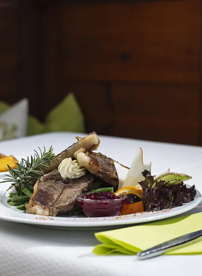 Ein Teller mit gebratenem Fleisch, Gemüse und einem Glas Rotwein auf einem weißen Tisch.