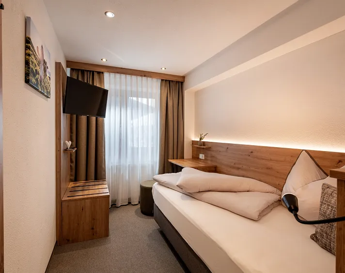 Gezellig ingerichte hotelkamer met een eenpersoonsbed, houten meubels en een flatscreen-tv aan de muur.