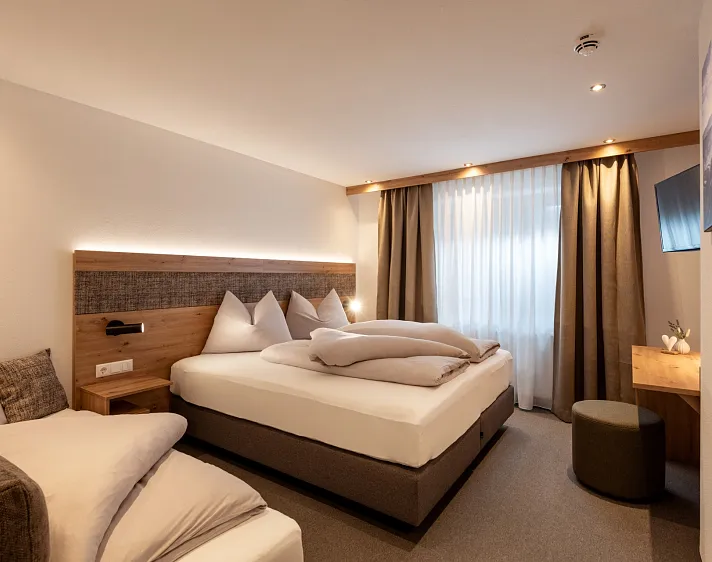 Modernes Hotelzimmer in Tirol mit einem Doppelbett, einem kleinen Tisch und einem Sessel.