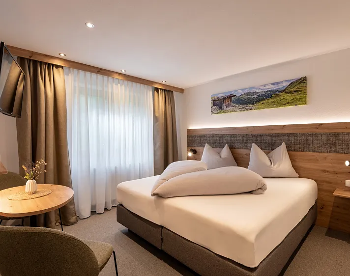 Hotelzimmer mit Doppelbett und Bergmotiv an der Wand.