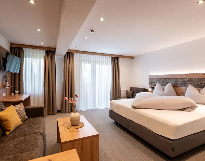 Modernes Hotelzimmer mit Doppelbett, Sofa und Tisch, neutral dekoriert.