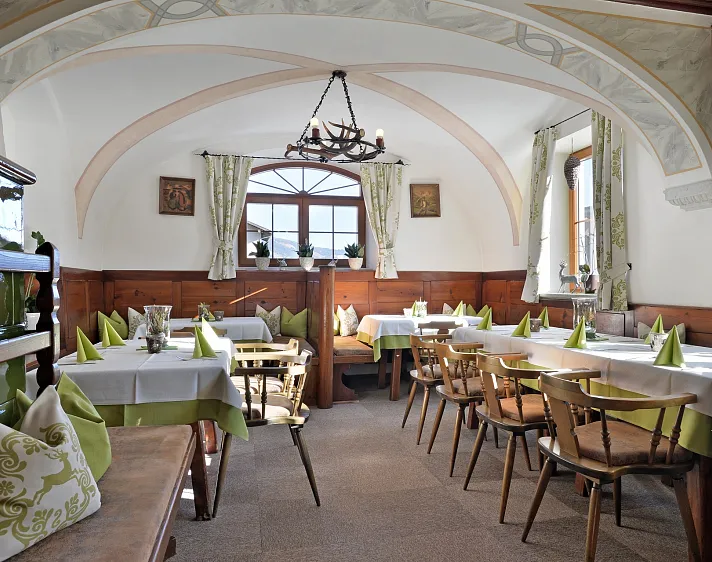 Gemütlicher Tiroler Gastraum mit Holzmöbeln, weißen Tischdecken und grünen Akzenten.