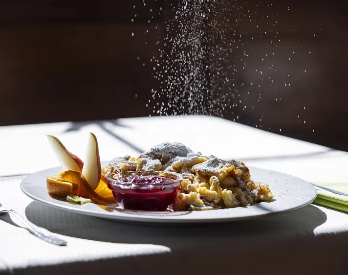 Kaiserschmarren mit Puderzucker und Kompott auf einem Teller serviert.