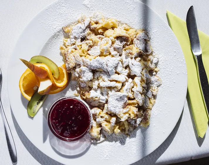 Kaiserschmarrn mit Puderzucker, Orangenscheiben, Kiwi und Marmelade auf einem Teller.