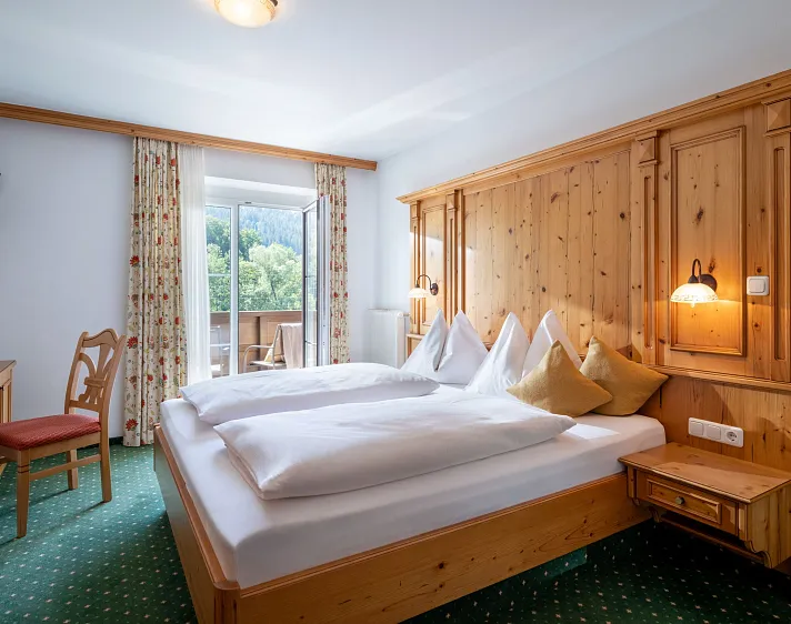 Knus hotelkamer met houten meubilair, uitzicht op bergen vanuit het balkon.