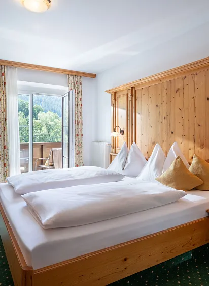 Hotelzimmer in Tirol mit Holzmöbeln, Bett, Schreibtisch und Blick auf bewaldete Berge.
