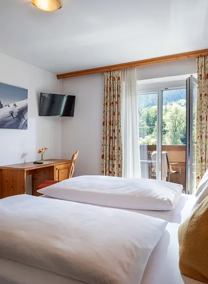 Hotelkamer met houten meubels, een bed, een balkon en uitzicht op groene bergen in Tirol.