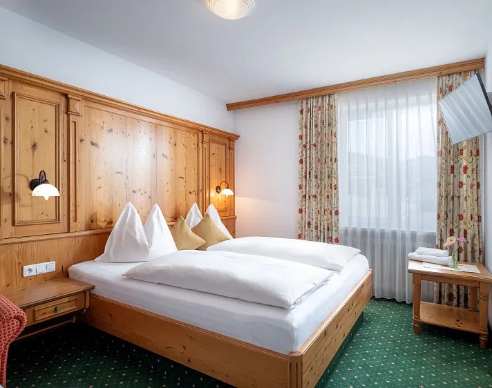 Knus hotelkamer met traditioneel houten meubilair en een groen tapijt, met een groot bed en een raam met uitzicht.