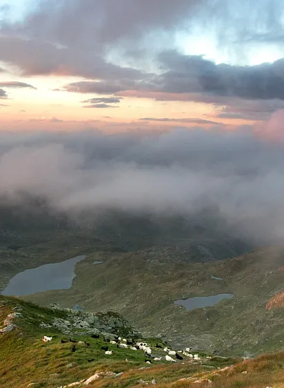 Blick auf eine Alpenlandschaft bei Sonnenuntergang mit Bergen, Wolken und mehreren Seen.