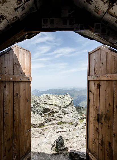 Berghütte mit offenem Holztor, Blick auf felsige Alpenlandschaft.