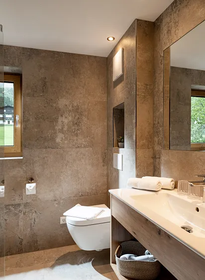Modernes Badezimmer mit freistehender Badewanne, großem Spiegel und Fenster mit Blick auf grüne Landschaft.