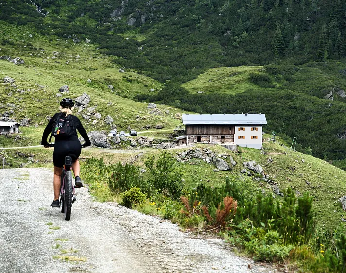Radfahrer auf alpinem Weg in den Tiroler Bergen mit Hütte im Hintergrund.