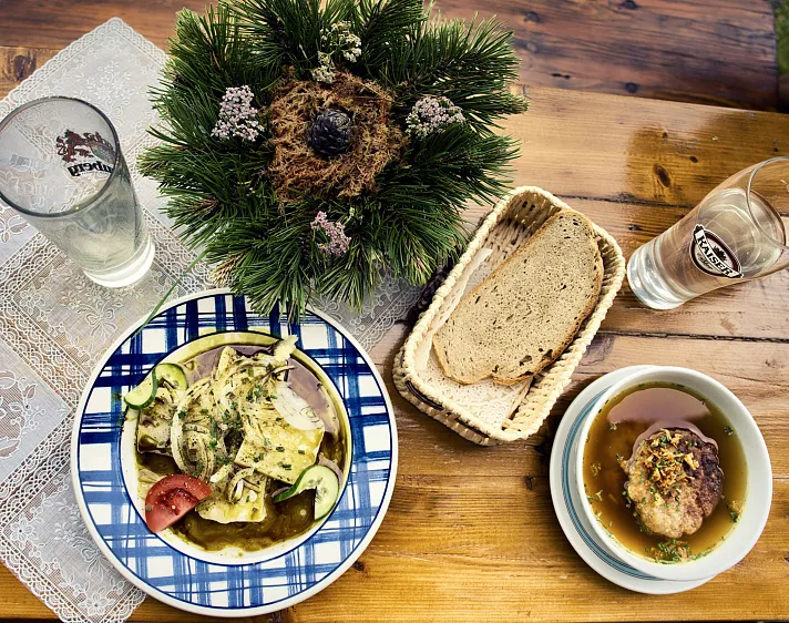 Traditionelle Tiroler Mahlzeit mit Suppe, Hauptgericht und Brot auf einem Holztisch.