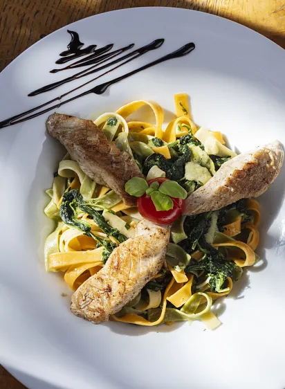 Ein Teller Tagliatelle mit gegrilltem Hähnchen und Gemüse.