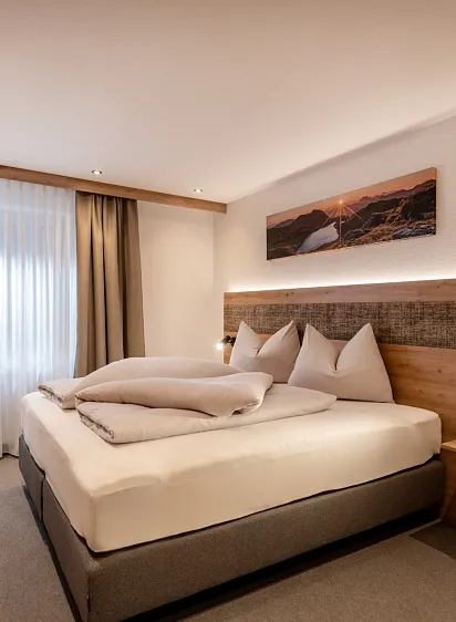 Modern eingerichtetes Hotelzimmer mit Doppelbett, Seitenfenster und Schreibtisch.