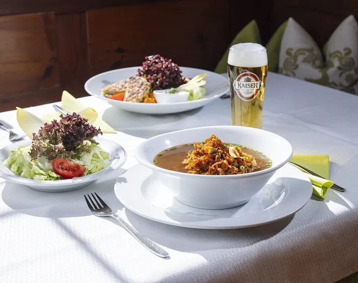 Zwei Teller mit Tiroler Gerichten und ein Glas Bier auf einem Tisch.