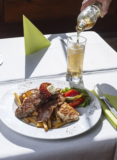 Ein Teller mit Fleisch, Pommes frites und Gemüse auf einem Tisch mit einem Getränk, das daneben eingeschenkt wird.
