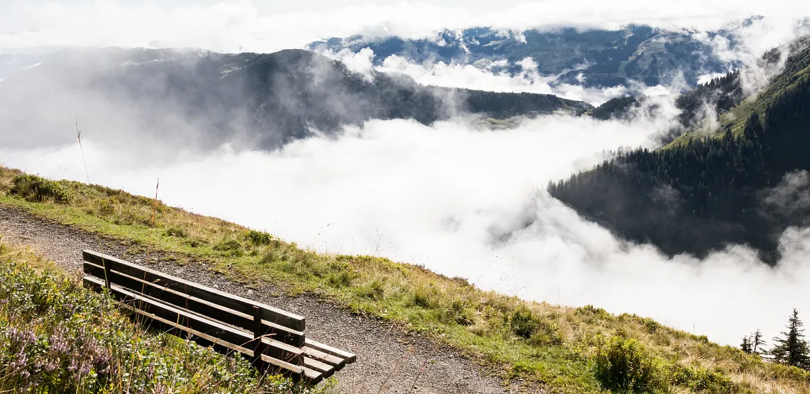 Mountain landscape with a bench overlooking a misty valley in the Alps.