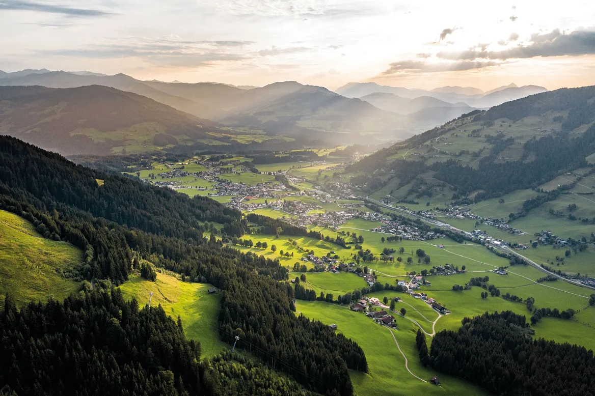 Luftansicht des Brixentals in Tirol, umgeben von grünen Wiesen und Bergen bei Sonnenuntergang.
