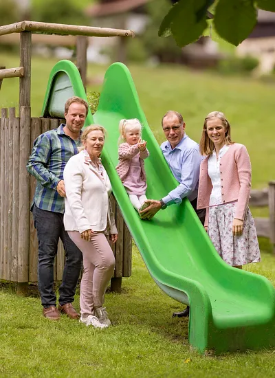 Familie auf einem Spielplatz mit Rutsche in Tiroler Landschaft.