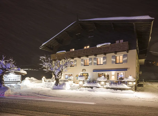 Ein verschneites Gasthaus in Tirol bei Nacht, umgeben von winterlicher Landschaft und beleuchtetem Eingangsbereich.